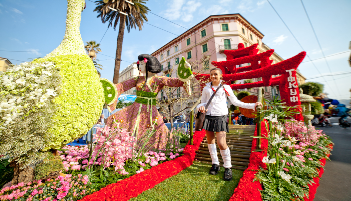 una-ragazzina-cammina-in-una-passerella-d-erba-attorniata-da-fiori-multicolore-e-dietro-lo-sfondo-di-un-tipico-palazzo-sanremese